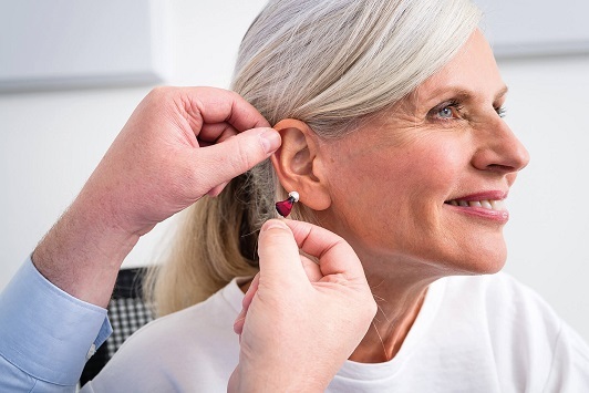 Ältere Frau bekommt ein modernes Hörgerät eingesetzt und lächelt zufrieden dabei.